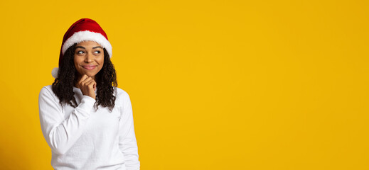 A young woman wearing a red Santa hat stands in front of a bright yellow background. She has a playful smile and looks thoughtfully to the side, suggesting a cheerful mood for the holiday season.