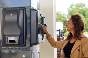 A middle-aged woman smiles as she selects the amount of gas to fill up at the gas station. © Inspiraciones