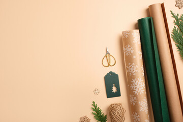 Gift wrapping background. Paper rolls, green gift tag, and gold stars on beige backdrop. Copy space for holiday text or design.