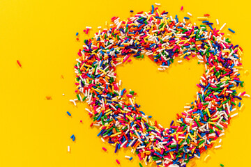 Sprinkles arranged in heart on yellow background