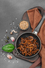 Fried Shimeji mushrooms with garlic, basil, and spices in a pan, served on a dark background
