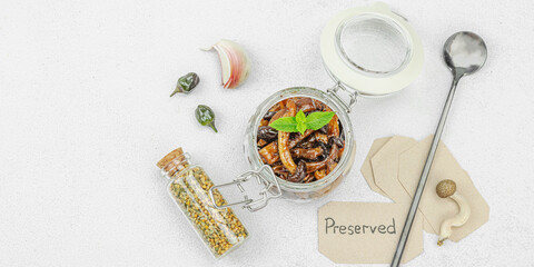 Preserved shimeji mushrooms in a glass jar with herbs and spices on a light background