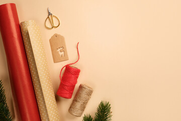 Christmas gift wrapping with red and brown wrapping paper, rope, labels, scissors, fir spruce on beige backdrop. Copy space.