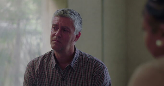 Close up of man expressing deep emotion during group therapy session, eyes slightly red as he opens up in quiet, supportive indoor space