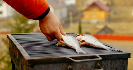 Professional chef carefully seasoning sea bream over open flame grill, showcasing outdoor culinary expertise with fresh Mediterranean seafood preparation