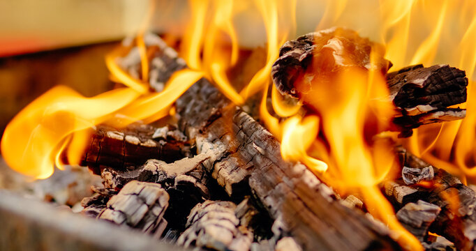 Wooden logs burning intensely in barbecue grill, generating bright orange flames and glowing red embers during outdoor cooking preparation