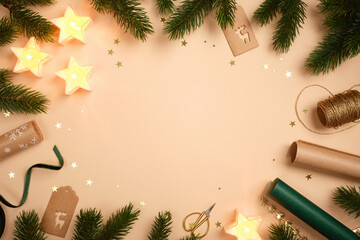 Christmas frame with star candles, fir branches, gift tags, and wrapping supplies on beige background. Copy space for text or design.