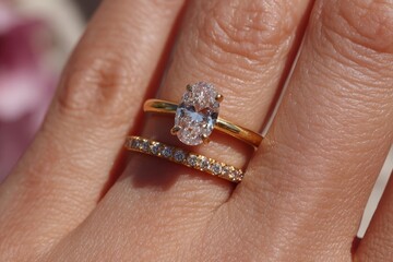 Woman's hand wearing gold engagement ring and diamond wedding band set. Use in designs related to weddings, engagements, anniversaries, and jewelry.