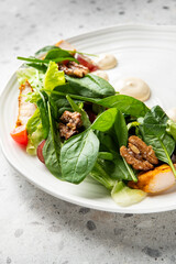 A vibrant chicken and spinach salad on a white plate, featuring walnuts, grapes, and a creamy dressing. The dish is presented close-up on a grey surface