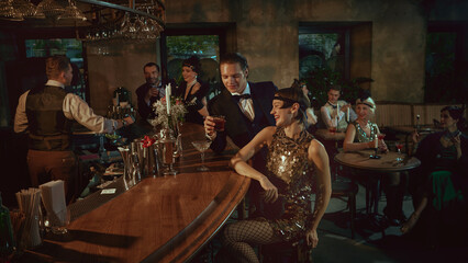 Stylish friends in vintage eveningwear sharing cocktails at the bar. Concept of bar promo, luxury alcohol visuals, nightlife marketing, event content, and festive holiday campaigns.
