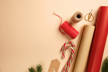 Christmas gift wrapping with red and brown wrapping paper, rope, labels, scissors, candy canes on beige backdrop. Copy space.