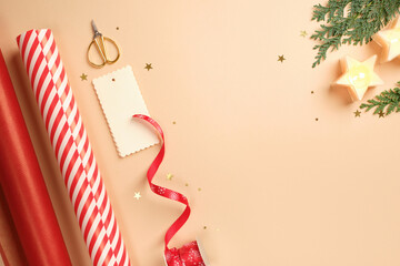 Christmas gift wrapping with red and white striped wrapping paper, ribbon, scissors, thuja spruce, candles on beige backdrop. Copy space.