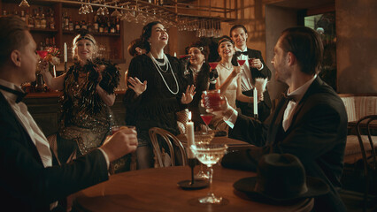 Retro party crowd laughing and celebrating with cocktails in stylish bar. Concept of nightlife...