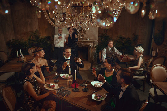 Retro dinner celebration with stylish friends toasting around festive table setting. Concept of New Year event visuals, gala dinners, creative posters, luxury bar and restaurant marketing.