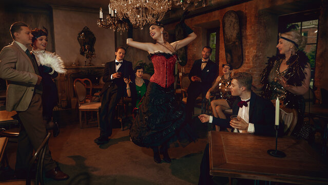 Glamorous retro dancer in red corset performing for stylish friends in vintage club. Concept of entertainment visuals, Christmas event marketing, luxury nightlife branding, themed retro promotions.