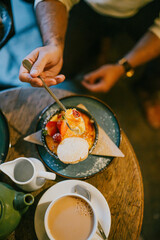 A person is eating a dessert with a spoon. The dessert is on a plate and there are other items on the table, such as a cup and a teapot. The scene appears to be casual and relaxed