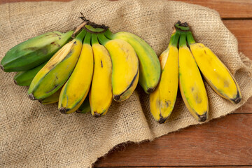 Bunches of ripe and partially green bananas displayed on a burlap sack and a wooden cutting board. Rustic still life emphasizing tropical and raw fruit ingredients.