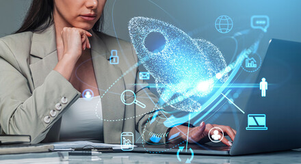 Woman in suit working on laptop with glowing rocket hologram and tech icons overlay, on office background, concept of innovation and startup strategy