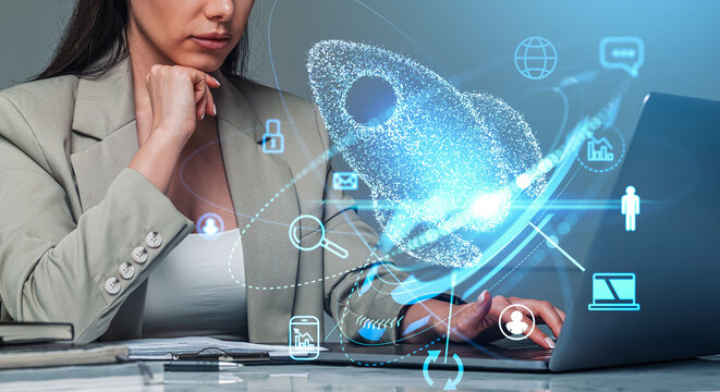 Woman in suit working on laptop with glowing rocket hologram and tech icons overlay, on office background, concept of innovation and startup strategy - Powered by Adobe