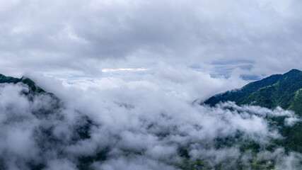 Aerial view of beautiful green mountain peaks covered by thick white clouds and mist.