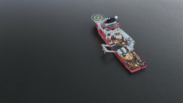 Aerial view of a red and white ship featuring a helipad on dark, still water, creating a striking contrast of industrial design against the natural backdrop, Poughkeepsie, New York, United States.