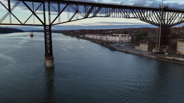 Aerial view of the Mid-Hudson bridge and the calm river, with a ship sailing in the distance under a cloudy sky, Poughkeepsie, New York, United States.