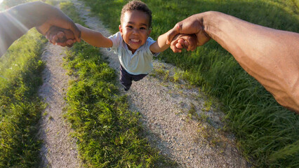 Point of view POV of a dad twirling his little son in a circle, holding his hands, enjoying cheerful family fun, outdoor play, and a carefree childhood.