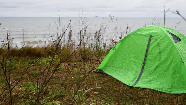 Green tent camping by Baltic Sea shore on overcast day