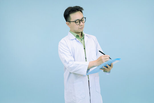 Confident Asian scientist or doctor in a lab coat and glasses, standing and  writing notes on a clipboard in blue studio background - Powered by Adobe