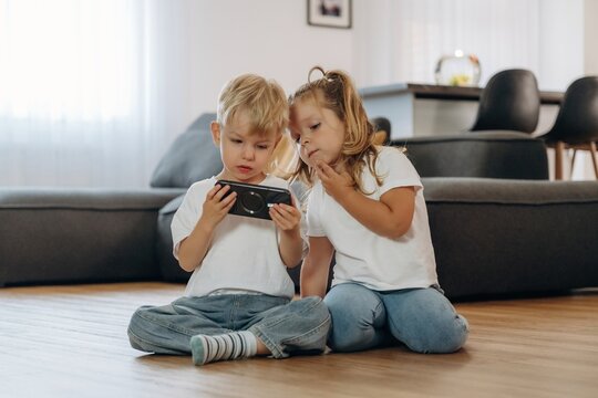 Smartphone in hands of boy. Little kids are playing together in the domestic room at daytime