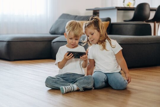 Smartphone in hands of boy. Little kids are playing together in the domestic room at daytime