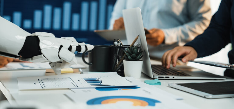 A dynamic business meeting scenario showcasing modern technology with a robot arm. Professionals engage in discussions while analyzing important data visualizations and documents.Noogenesis - Powered by Adobe