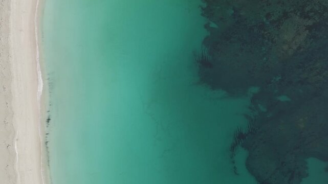 Aerial view of the contrasting turquoise sea meeting the pale sandy beach with dark patches, creating a stunning coastal scene, Leknes, Nordland, Norway.