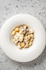 A close-up shot of delicious, creamy mushroom gnocchi served in a white bowl. The dish features soft potato dumplings, sliced mushrooms, and a rich, white cream sauce, garnished with herbs.