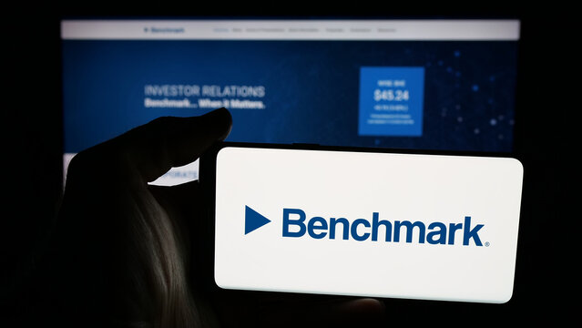 Stuttgart, Germany - 11-13-2025: Person holding mobile phone with logo of US company Benchmark Electronics Inc. on screen in front of web page. Focus on phone display.
