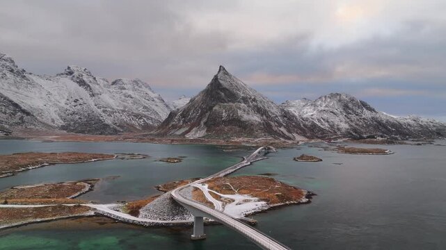 Aerial view of Fredvang Bridges cutting across the turquoise waters, against a backdrop of snow-capped mountains, Fredvang, Nordland, Norway.
