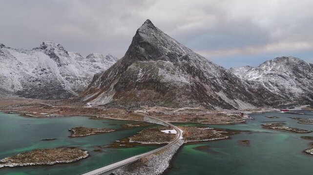 Aerial view of the Fredvang Bridges amidst snow-capped mountains and turquoise waters, creating a stunning contrast of cold and warm tones, Fredvang, Nordland, Norway.