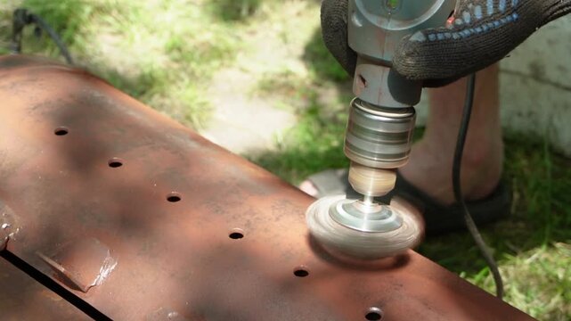 A worker removes rust and corrosion from a metal surface using a wire brush attachment on an electric drill
