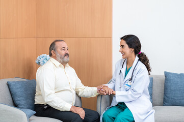 Obraz premium Female doctor in white medical coat and patient discussing something, holding his hand and smiling while sitting on sofa. Medicine and health care concept. Doctor and patient.