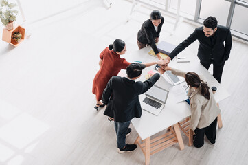 Business team putting hands together in unity during a meeting, symbolizing teamwork, collaboration, partnership, and success in a modern office environment.