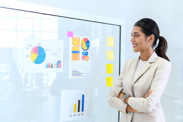 young modern businesswoman in smart casual using sticky notes for strategy ideas while standing behind the glass board in the board room at the office. Business project planning. Hard choice to make.