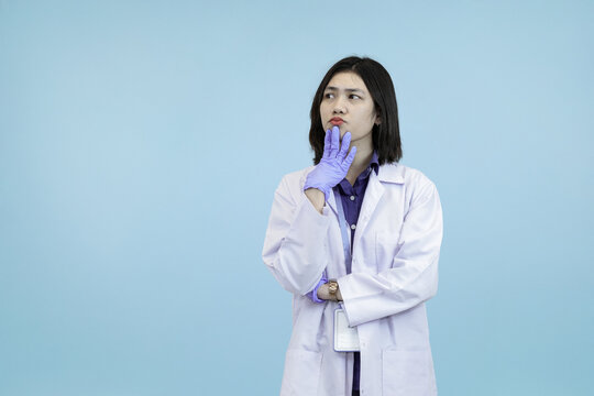 An Asian female scientist or doctor in a lab coat, wear a gloved symbolizing deep thought, skepticism, or problem-solving strategy in blue studio background