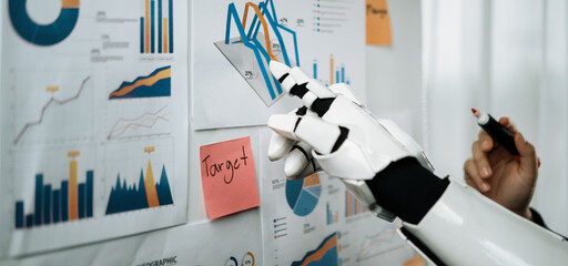 A sleek robot hand points at various business charts and graphs displayed on a wall, emphasizing key data targets and strategic insights for effective decision making.Noogenesis