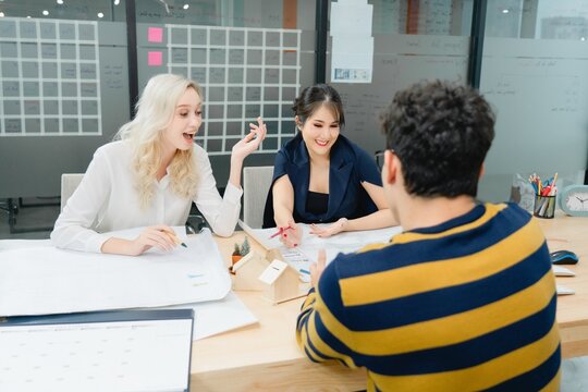 Two female colleagues excited engagement discussing creative, male professional during an energetic meeting. collaborating on architectural blueprints, design concepts, strategic innovation in office