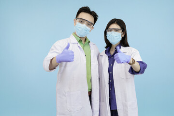 Cheerful Asian science professionals giving enthusiastic thumbs-up gestures, symbolizing success, approval, or excellent research results in blue studio background