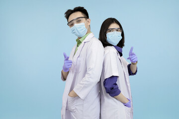 Confident Asian medical professionals in lab coats and safety gear, standing back-to-back, symbolizing strong teamwork and healthcare in blue studio background
