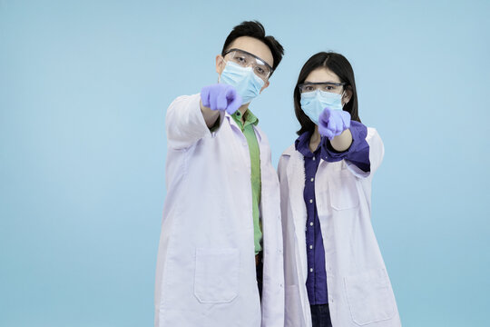 Asian medical pointing directly at the camera, symbolizing recruitment, public warning, or shared health responsibility in studio blue background