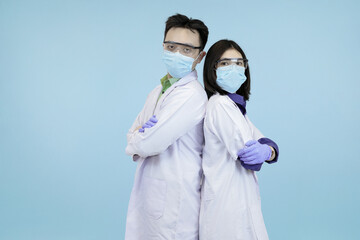 Confident Asian medical professionals in lab coats and safety gear, standing back-to-back, symbolizing strong teamwork and healthcare in blue studio background
