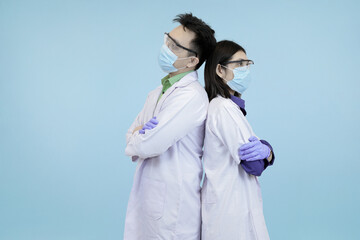 Confident Asian medical professionals in lab coats and safety gear, standing back-to-back, symbolizing strong teamwork and healthcare in blue studio background