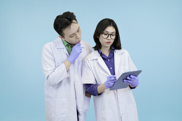 Pensive Asian science professionals closely examining data on a digital tablet, symbolizing focused analysis and problem-solving during research in studio blue background
